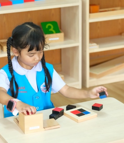 เด็กหญิงฝึกสมาธิกับบล็อกไม้มอนเตสเซอรี่ในห้องเรียนที่จัดสภาพแวดล้อมเตรียมพร้อม
