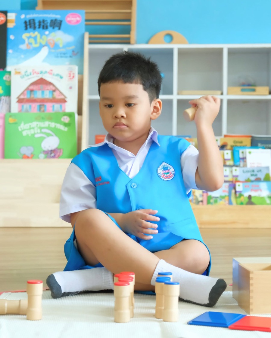กิจกรรมมอนเตสเซอรี่: น้องชายชุดนักเรียน MAS จดจ่อกับ Knobbed Cylinders อุปกรณ์ประสาทสัมผัสมาตรฐาน